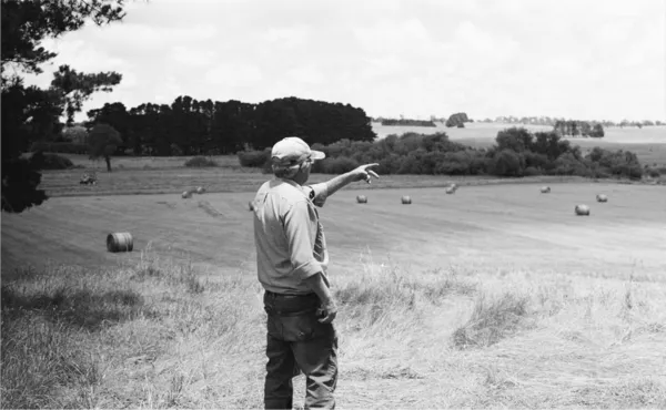 Un agricultor parado en un campo, señalando fuera de pantalla.